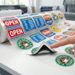 Double sided UV DTF decals gang sheet roll on a white surface, showcasing multiple 5-layer blockout window stickers printed on a transparent transfer film with a glossy finish, demonstrating 100% opacity.