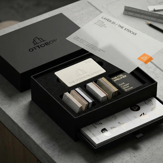 The full unboxing reveal of the OTTORON Midnight Industrial Master Sample Kit, showcasing the open matte black rigid box with double-layer black EVA foam, revealing premium cards, the Foil Specifier, the Adhesive Archive swatch book, and the $20 debossed credit card resting on top.